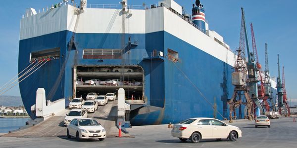 Cars disembarking from a large blue cargo ship at a port.