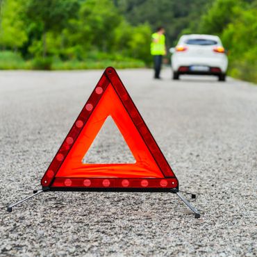 Red emergency triangle on road with person and white car in background.