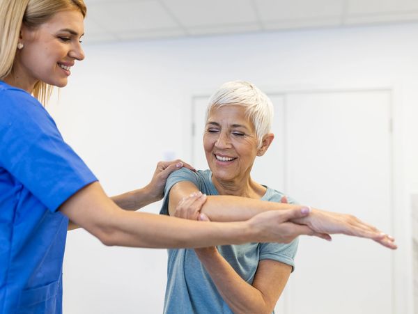 Physical therapist assists elderly woman with arm stretch exercises.