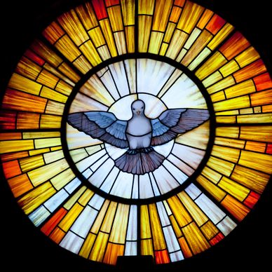 Stained glass window with a dove and radiant yellow-orange rays.