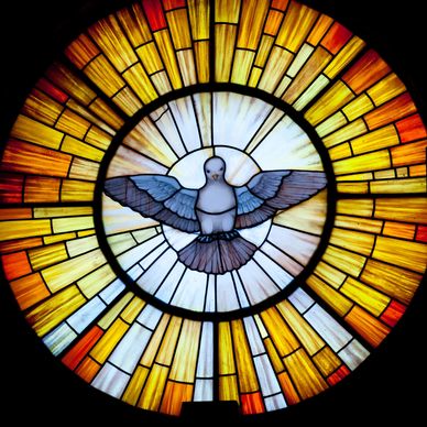 Stained glass window with a dove and radiant yellow-orange rays.