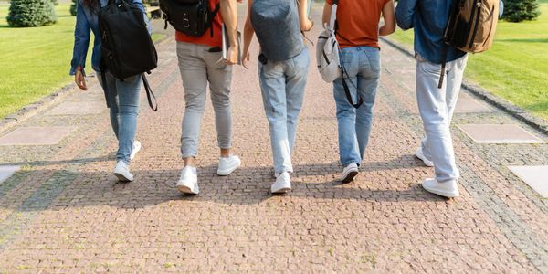 Five people with backpacks walking on a paved path outdoors.
