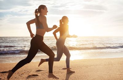 Dos mujeres corriendo en la playa al atardecer.