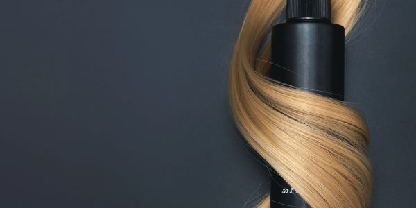 Black bottle wrapped with blonde hair on dark background.