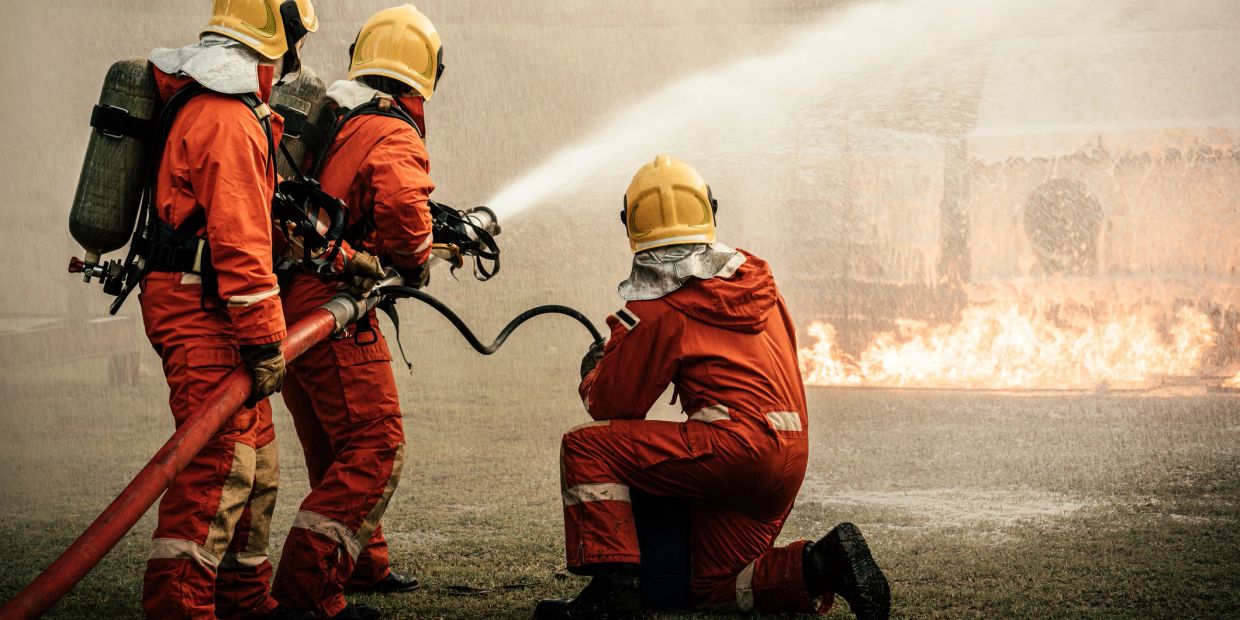 Tres bomberos luchan contra un incendio con manguera contra incendios.