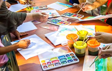 Children painting with watercolors on paper at a table.