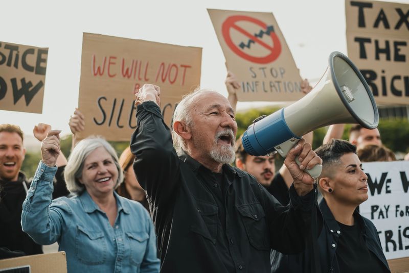 Crowd of people protesting against economic situation with carton placards and shouting to megaphone with raised arms during demonstration
