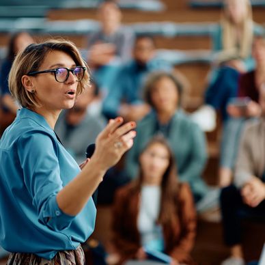 Woman speaking confidently to an attentive audience in a lecture hall.