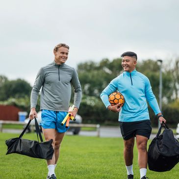 Two men carrying sports bags, one holding a soccer ball.