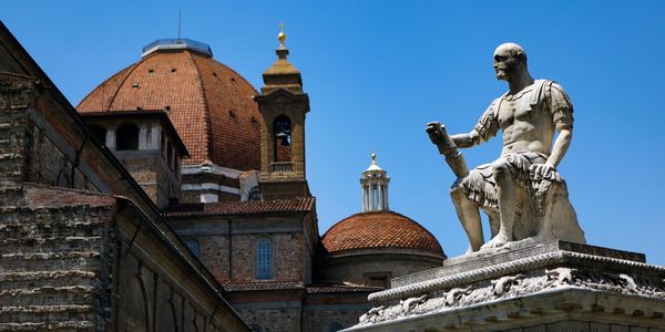 Historic statue and architecture in Florence, Italy, with a clear blue sky in the background.