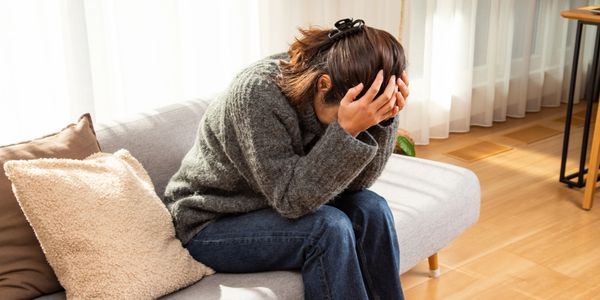 Person sitting on a couch, holding their head in distress.