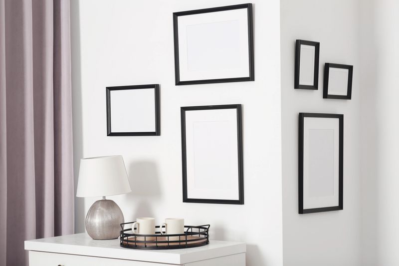 Empty frames hanging on white wall, cups and lamp indoors