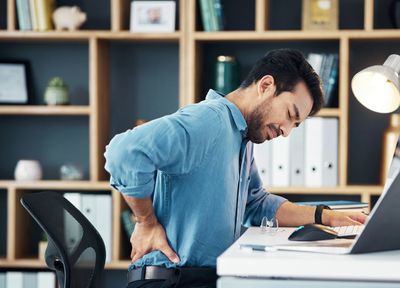 Man holding his lower back in pain while sitting at a desk.