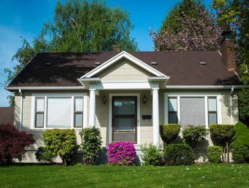 Small beige house with a brown roof and neatly trimmed bushes.