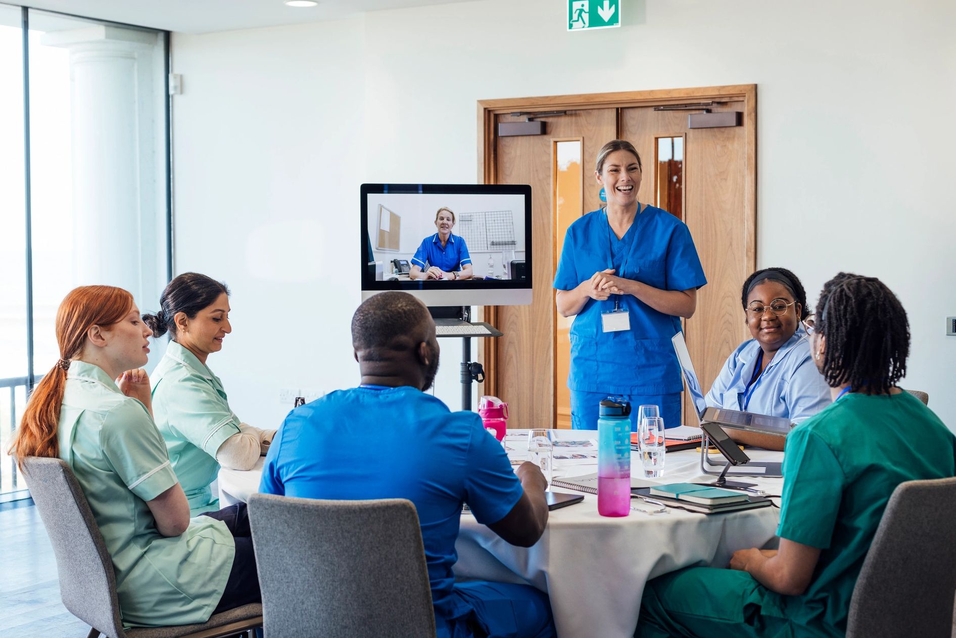 Healthcare professionals in a meeting with one presenting and another joining via video call.