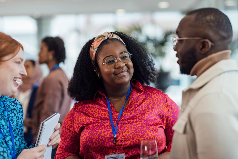 A close up view of a group of mixed age professionals who are taking advantage of a networking opportunity at a business conference in the North East of England. One woman is smiling at a new business acquaintance she is wearing a brightly coloured blouse and is wearing stylish round spectacles.