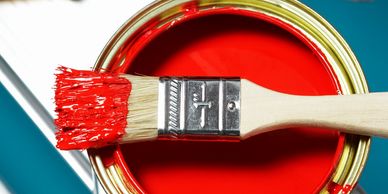 Open can of bright red paint with brush resting across the rim, ideal for home painting projects.