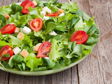 Fresh green salad with tomatoes, croutons, and cheese cubes on a wooden table.
