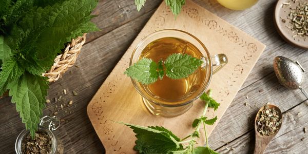 A cup of herbal tea with fresh green leaves on a wooden table.