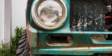 Close-up of an old, rusty turquoise off-road vehicle front with large tire.