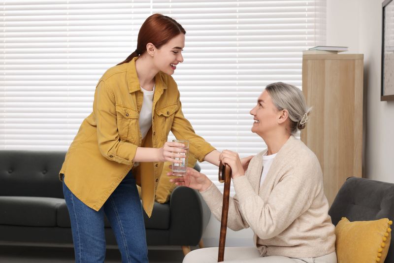 Caregiver giving water to senior woman with walking cane at home