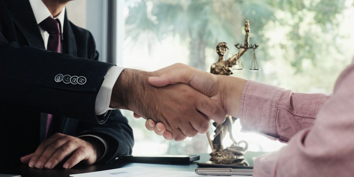 Two people shaking hands over a legal desk.