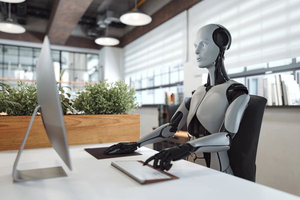 A humanoid robot working on a computer in a modern office.