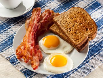 Breakfast plate with bacon, fried eggs, and toast.