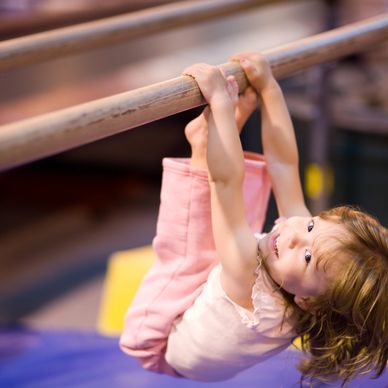 A young girl happily hanging upside down on a wooden bar.