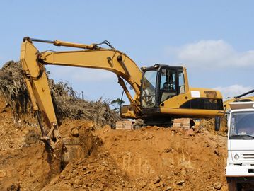 Yellow excavator digging earth at construction site beside a white truck.