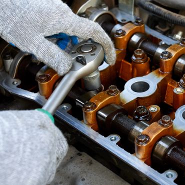 Gloved hands using a ratchet wrench on an engine camshaft.
