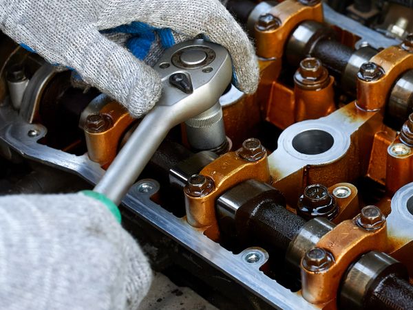 Gloved hands using a ratchet wrench on an engine camshaft.