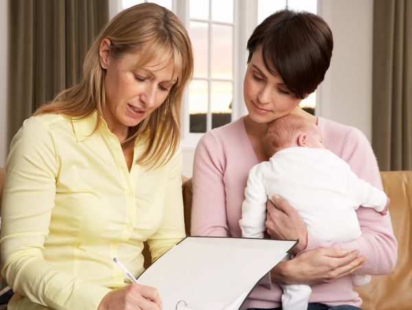 Two women discussing with a baby in arms, looking at a document.