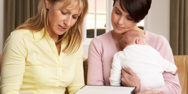 Two women discussing with a baby in arms, looking at a document.