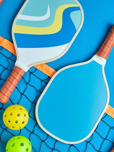 Colorful pickleball paddles and balls arranged on a blue court with a net.