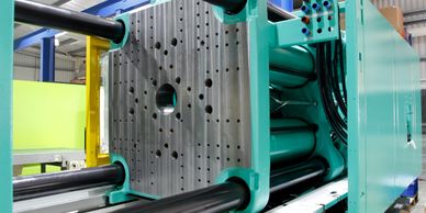 Close-up of an industrial injection molding machine with metal plates and hydraulic cylinders.