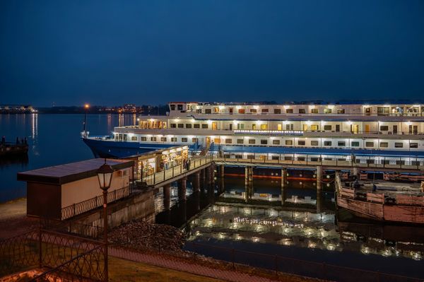 A lit-up cruise ship docked at night with reflections in the water.
