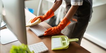 Person cleaning a computer desk with gloves.