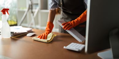Person cleaning a computer keyboard and desk with gloves and a cloth.