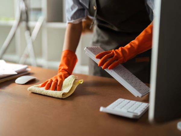 Person cleaning a keyboard and desk with gloves.