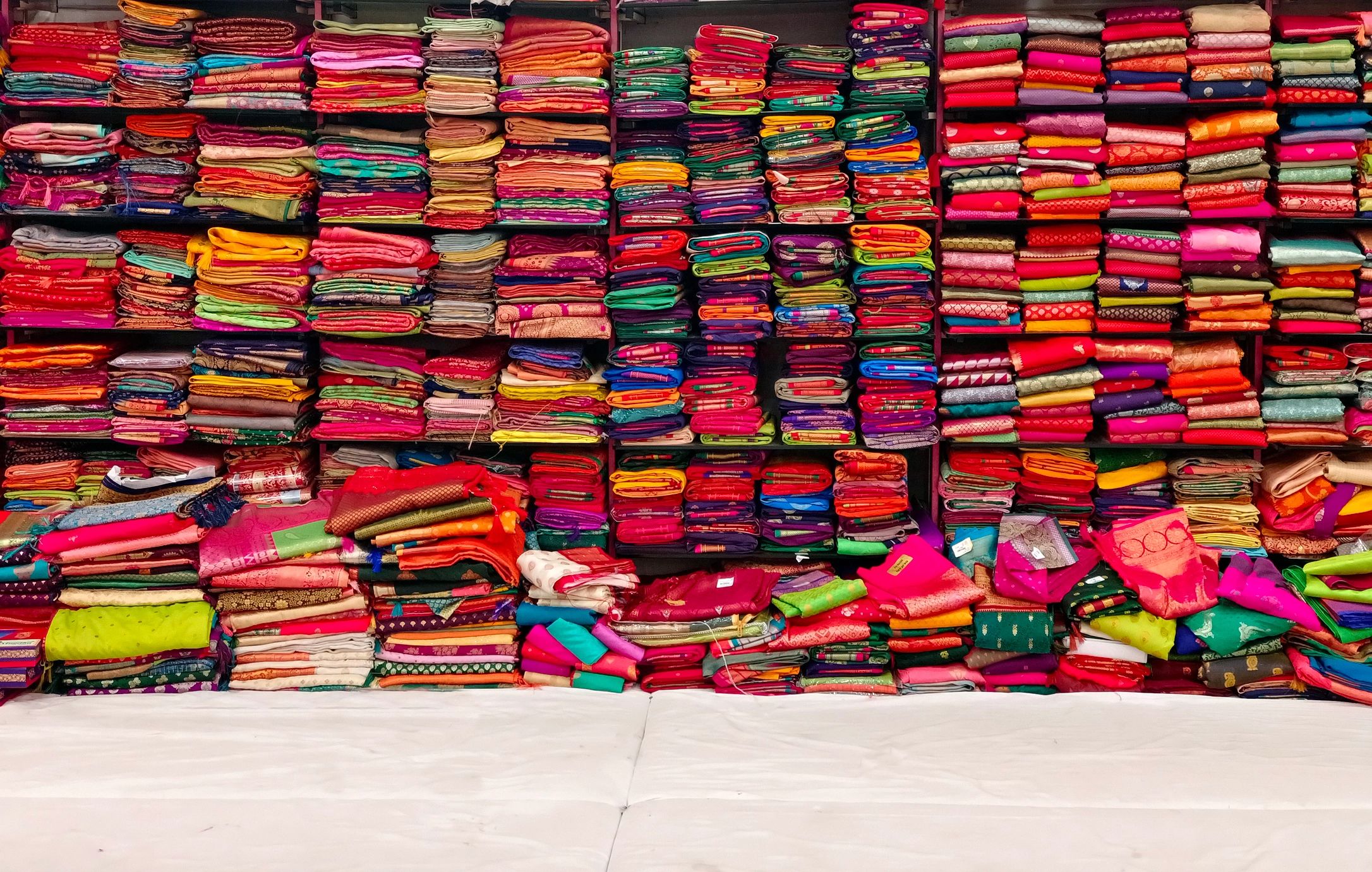 Stacked colorful folded fabrics on shelves.