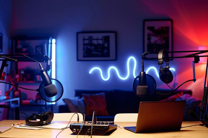 Laptop surrounded by microphones with headphones and soundboard standing on workplace of modern radio presenter in studio
