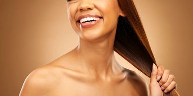Smiling woman holding her smooth, shiny hair against a warm brown background.