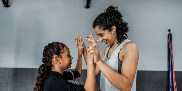 A woman and a girl smiling and playing hand games indoors.