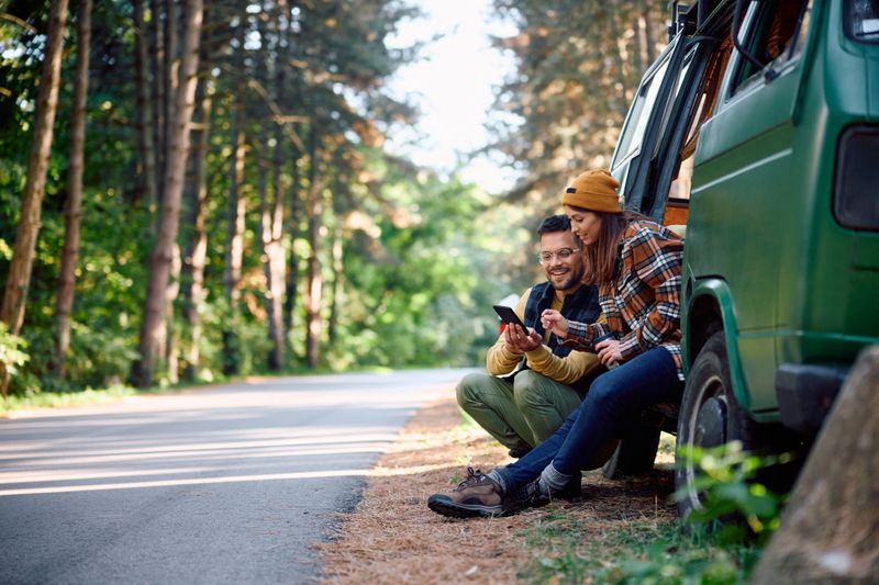 Young couple of campers using mobile phone while traveling with their van in nature. Copy space.