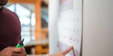 Person pointing at a date on a calendar.
