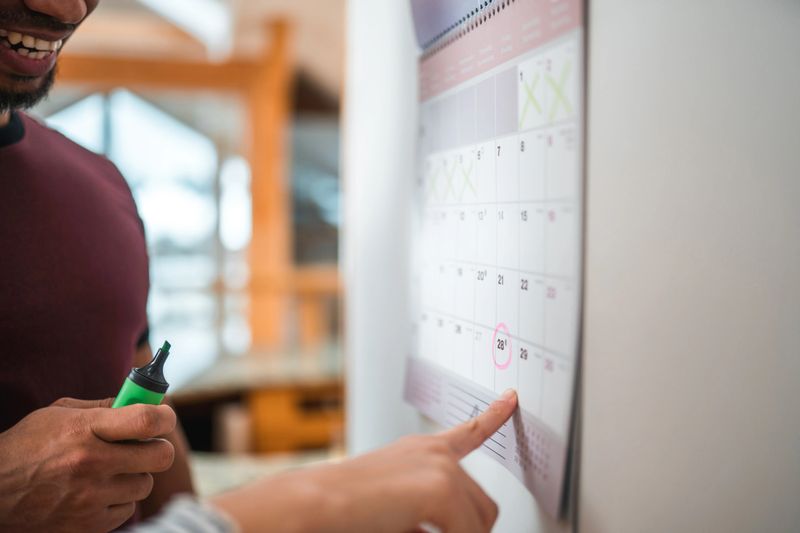 Close-up shot of a pregnant female pointing at a calendar. She is talking with her husband. They are happy and smiling.