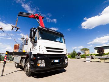 White truck with a red crane arm parked on a sunny industrial site.
