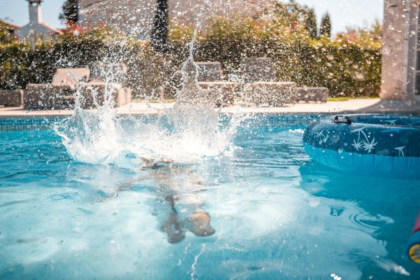 Splash of water as someone jumps into a pool on a sunny day.