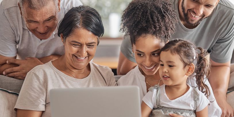 A joyful multi-generational family gathered around a laptop, sharing smiles and connection.